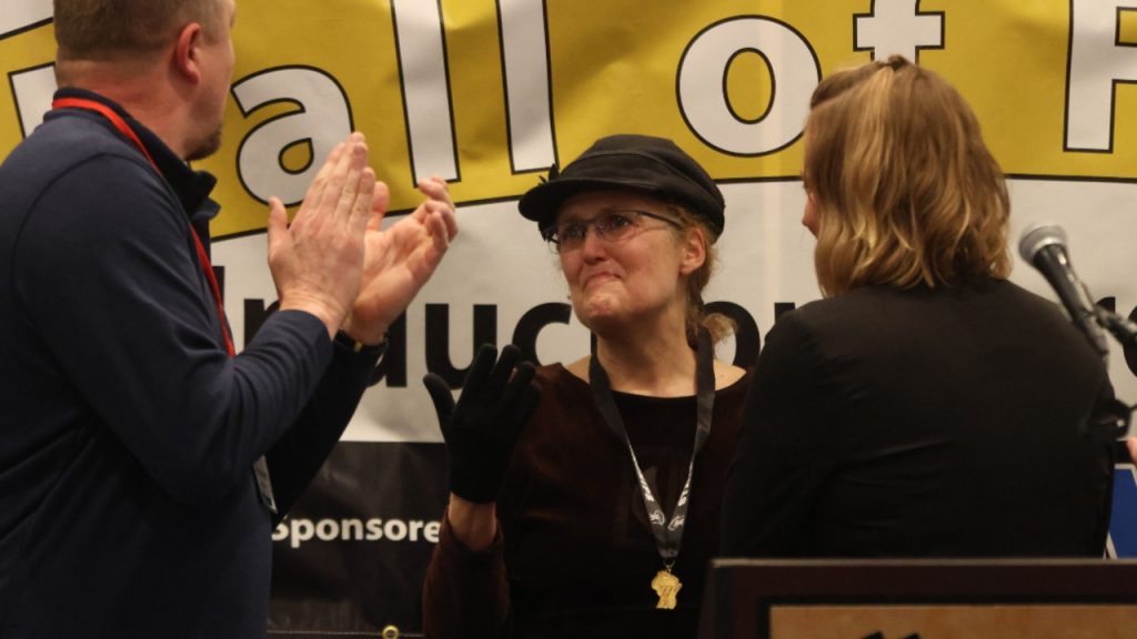 Maggie Flanagan, center, reacts after being presented with a gold medal honoring her father Patrick Flanagan’s 1945 Class B state shot put championship by WIAA assistant director Melissa Gehring at the Wisconsin Track Coaches Association Hall of Fame induction ceremony on Saturday at the Marriott Madison West in Middleton.